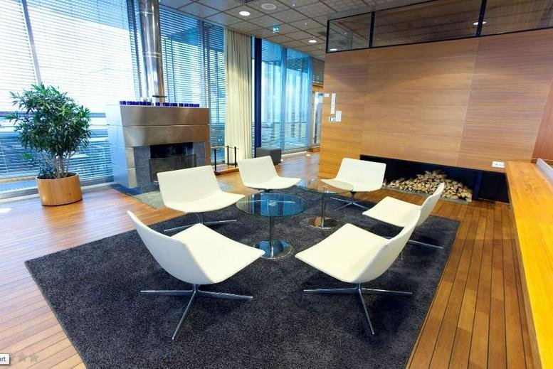 Lounge area at Teknobulevardi 3-5, Vantaa, Finland with white chairs, a glass table, and a modern fireplace.