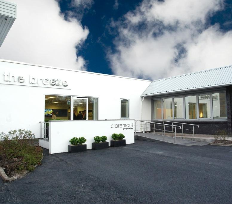 Exterior view of the white building at The Breeze at Claremont House with accessible ramp and greenery.