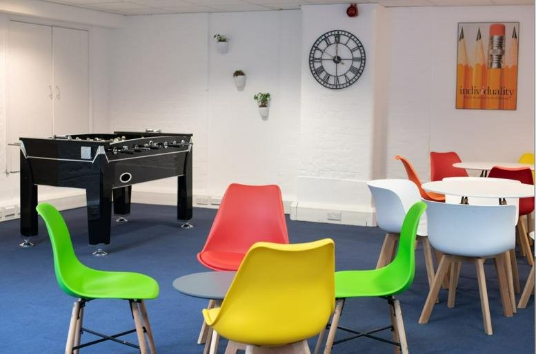Spacious communal breakout room with a foosball table and colorful Eames-style chairs.