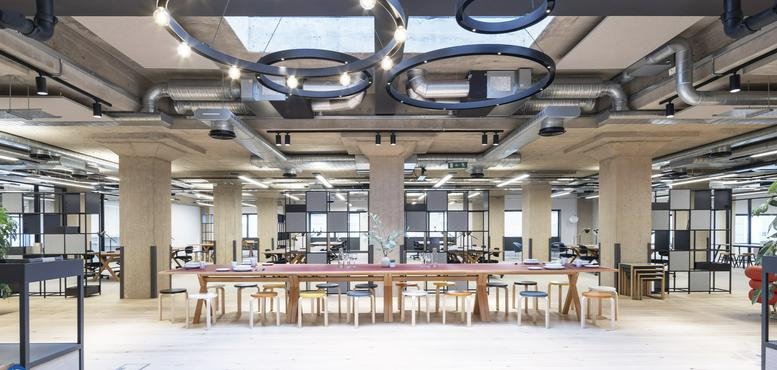 Spacious industrial-style communal area with a long wooden table and round pendant lights.