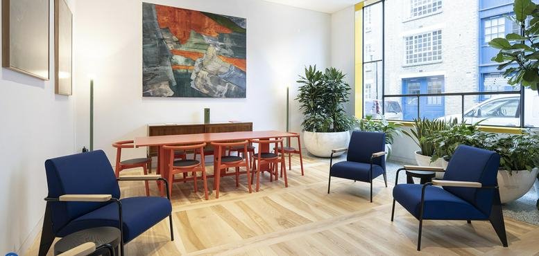 Sunlit breakout room with navy armchairs, a wooden table, and vibrant art.