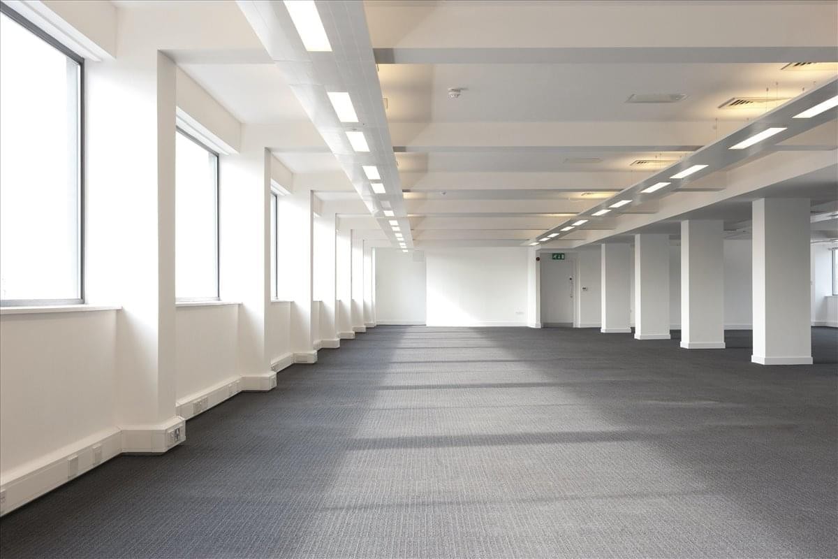 Bright, open-plan empty office space with grey carpeting and large windows.