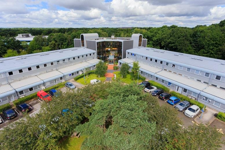 Aerial view of the modern H-shaped exterior of The Genesis Centre surrounded by lush greenery.