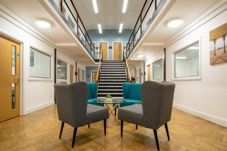 Spacious communal lounge at The Knoll Business Centre with grey wingback chairs and mezzanine walkways.