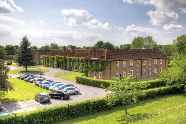 Wide view of the grand brick building with ivy-clad walls and a paved parking area.