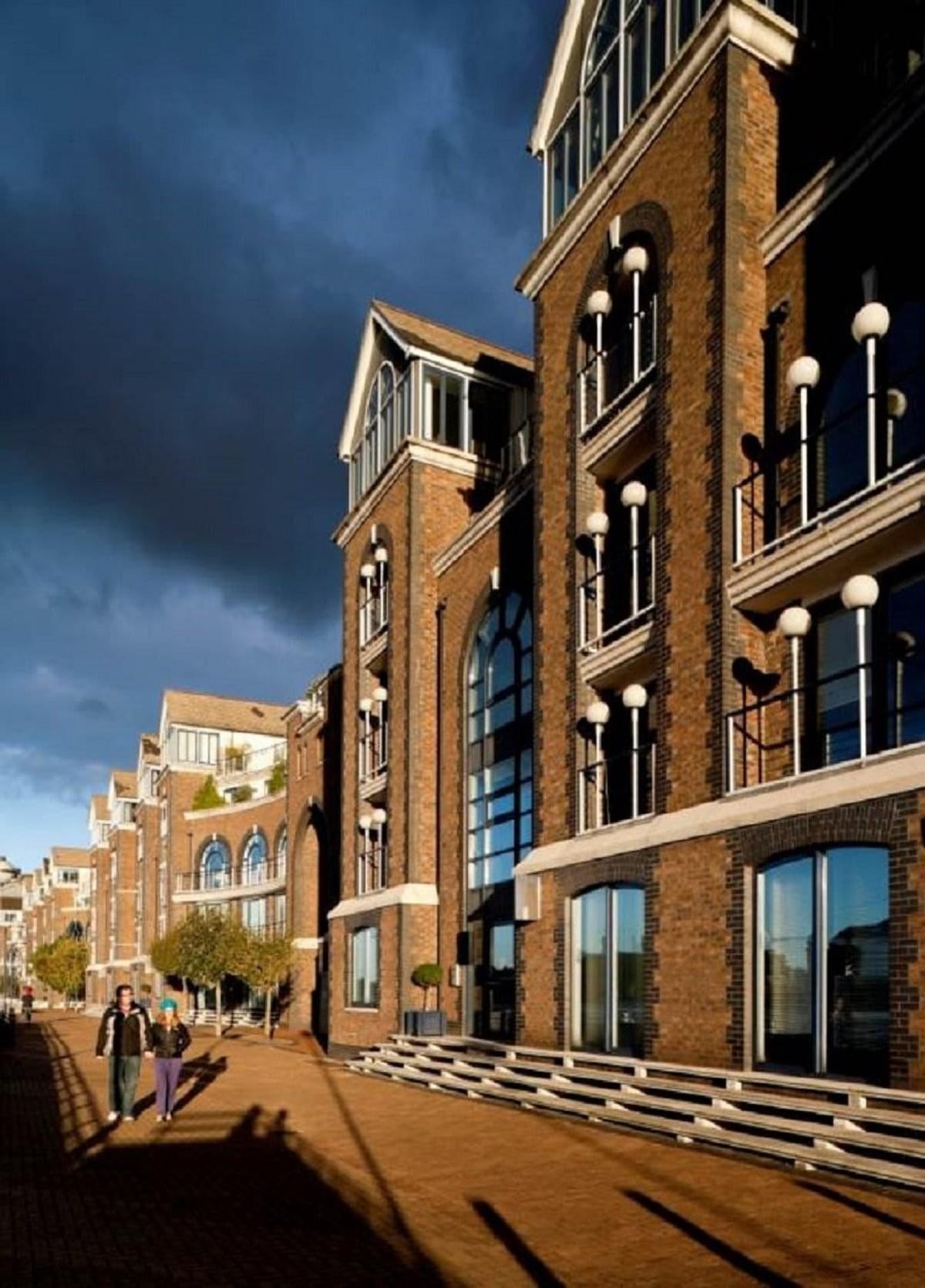 Grand brick facade of The Plantation Wharf, York Road with arched windows under a dramatic sky.