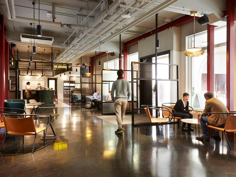 Spacious communal lounge with polished floors, leather armchairs, and a cafe area in the background.