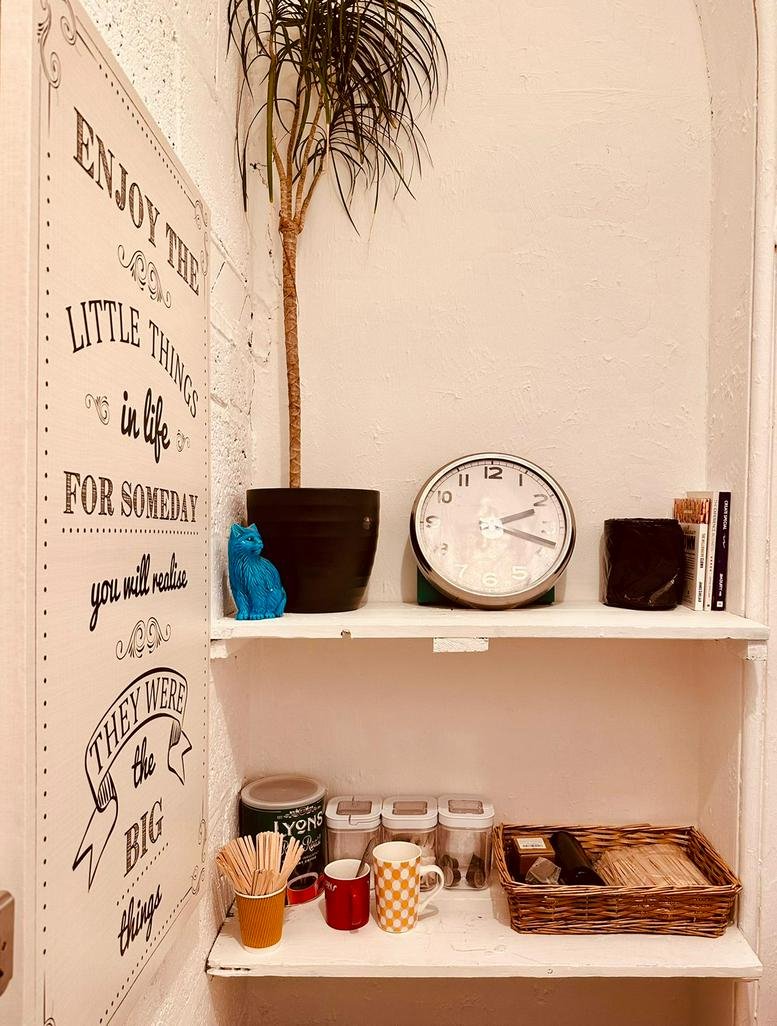 Tea and coffee station with wooden shelves, a potted plant, and a large motivational wall sign.