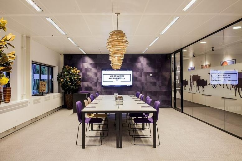 Modern conference room featuring a long white table, purple chairs, and a unique pendant light.