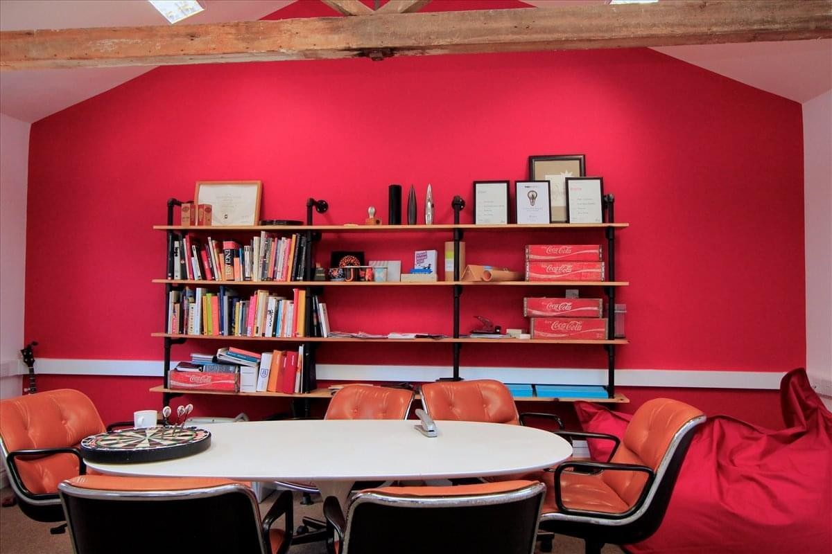 Communal lounge area at Thrales End Farm featuring a bold red feature wall, bookshelves, and orange chairs.