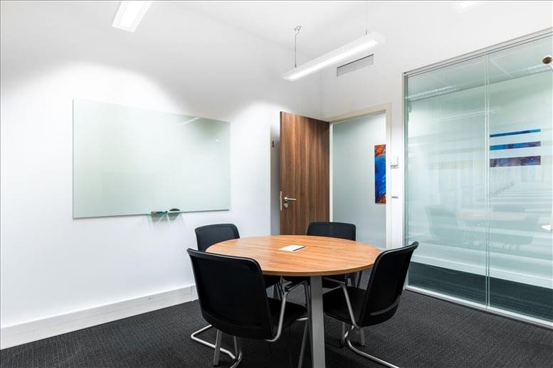 Bright, modern meeting room with a round wooden table, four black chairs, and a glass whiteboard.