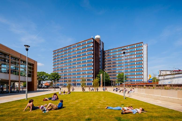Exterior view of Trafford House, Chester Road showing the building and a green lawn with people relaxing.
