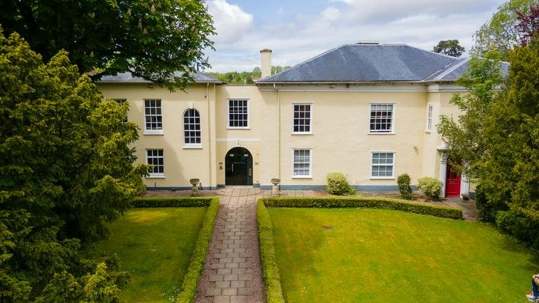 Exterior view of the historic Trym Lodge, 1 Henbury Road, Bristol, featuring yellow facade and manicured lawn.