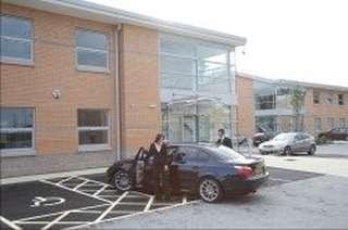 Contemporary office building entrance with a glass-fronted atrium and parking area.