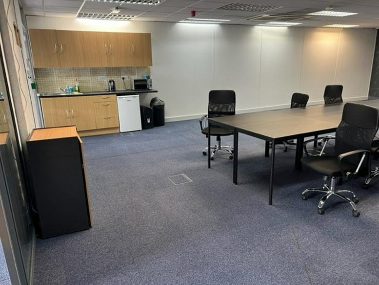 Spacious meeting room at Minerva Business Centre with a long conference table and kitchenette.