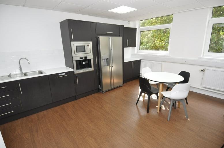 Spacious communal kitchen at Unit 6, Mostyn Road Business Park featuring dark cabinetry and a dining table.