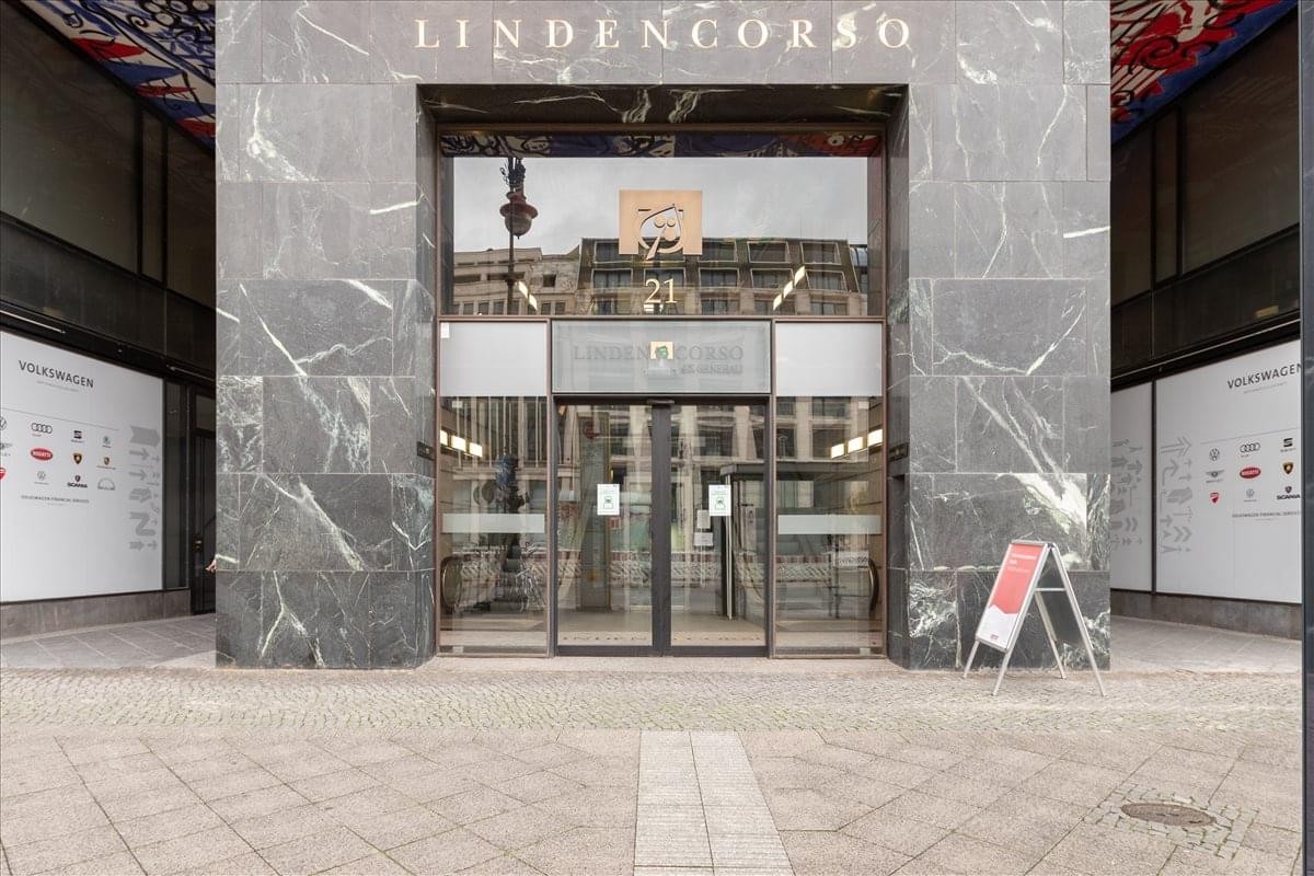 Entrance to the Lindencorso building showing the grey stone facade and glass revolving doors.
