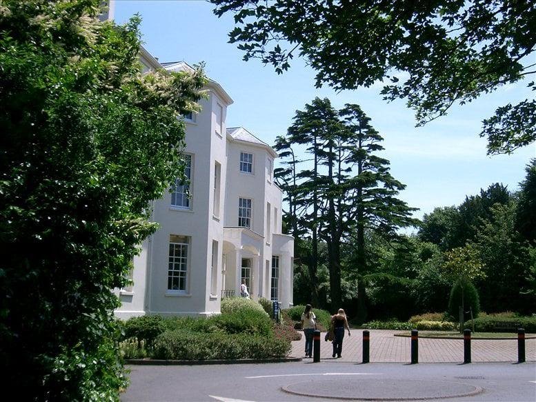 Bright white period building surrounded by lush green trees and manicured lawns.