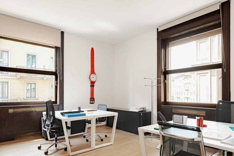 Spacious two-person office suite at Via Dogana 3 (3rd and 6th floor), Milan, Italy with large windows and a red wall clock.