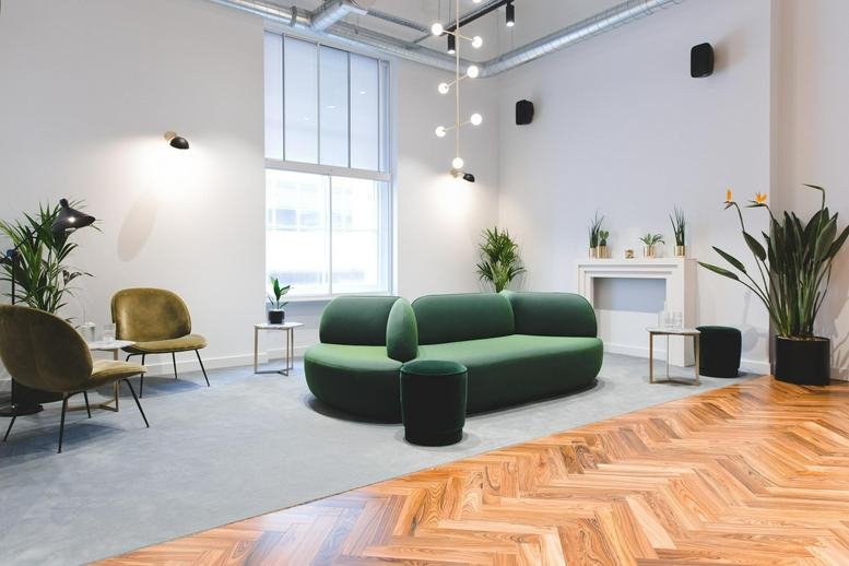 Bright lounge area with a curved green sofa, velvet armchairs, and herringbone wood flooring.