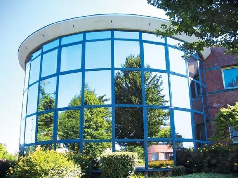 Curved glass exterior of Villeneuve d'Ascq, 1-3 Allée Lavoisier reflecting trees and blue sky.