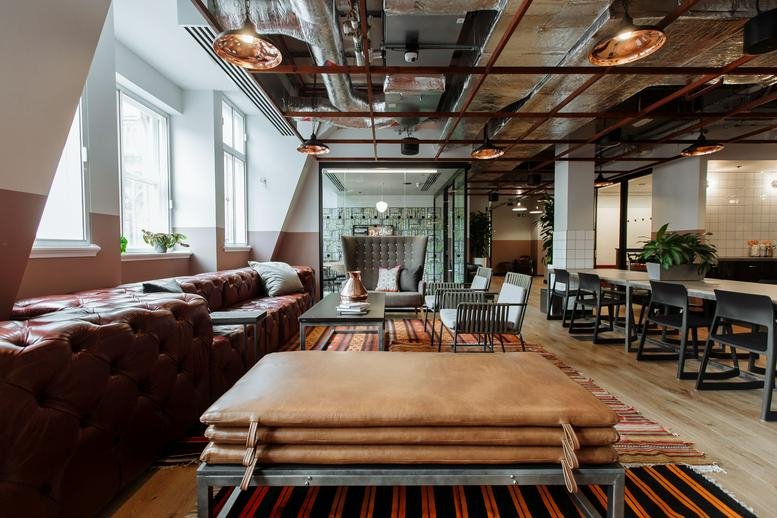 Spacious lounge with tufted leather sofas, warm lighting, and exposed ceiling pipes.