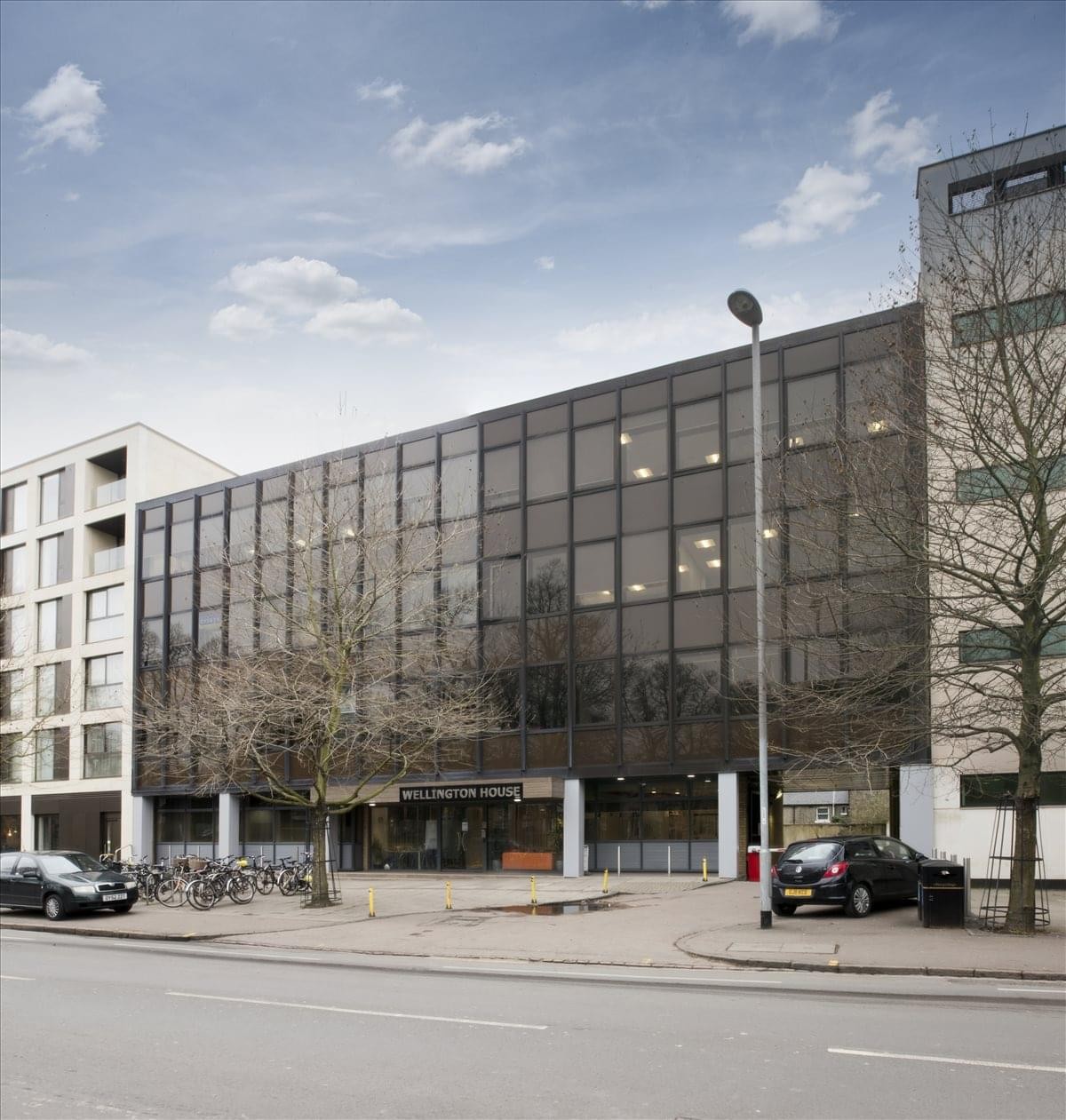 The dark-framed glass facade of Wellington House with a modern exterior and bicycle parking.