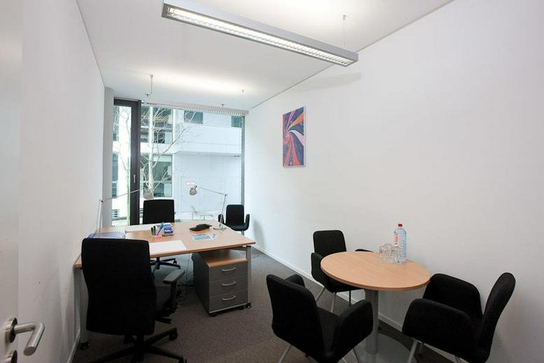 Bright office suite featuring a large desk and a separate round meeting table with black chairs.