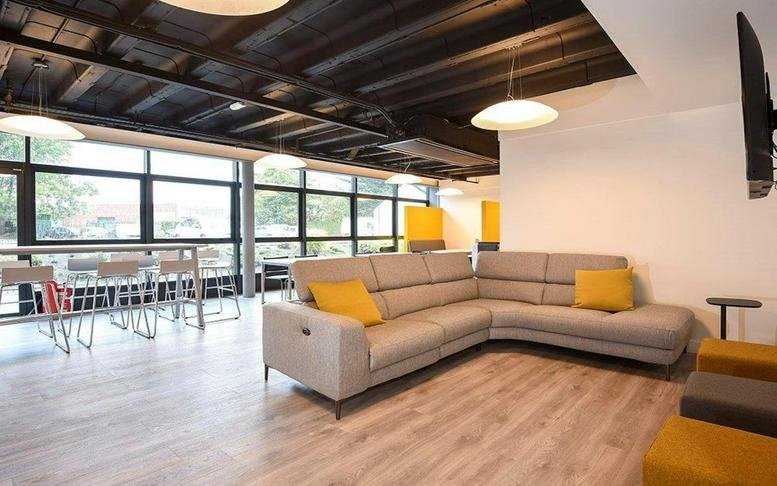 Spacious communal lounge with a grey sectional sofa, yellow cushions, and wood-style flooring.