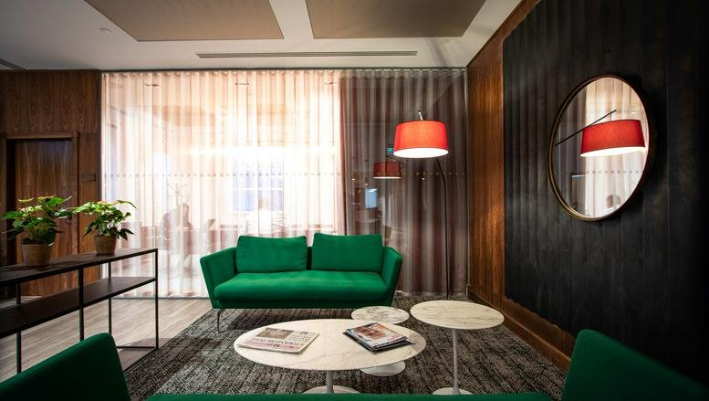 Lounge area with green sofa, round tables, and a red lamp.