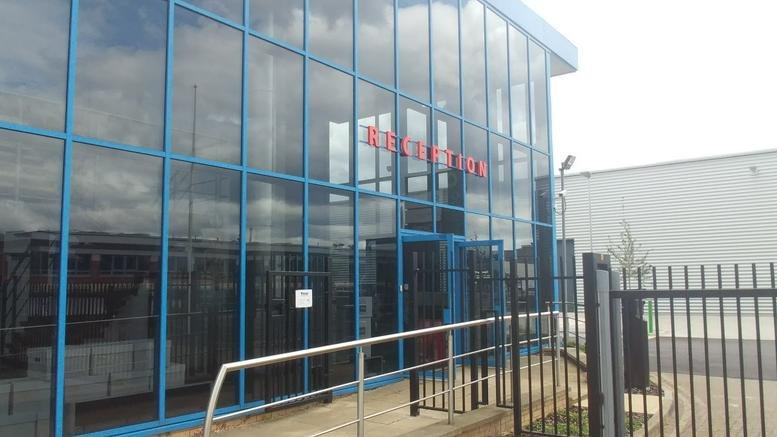Glass-facade exterior of Orchard Business Park on Forsyth Road with red reception signage.