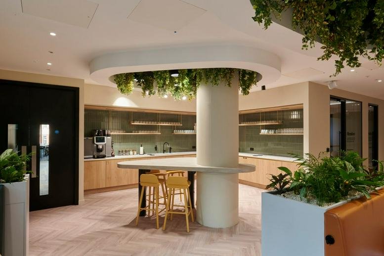 Spacious communal kitchen and breakout area at Orchard Place, London with a central island and hanging plants.