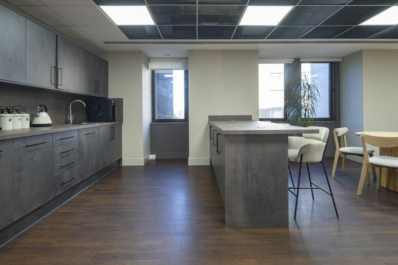 Modern office kitchen with sleek grey cabinetry and a breakfast bar with high-top seating.