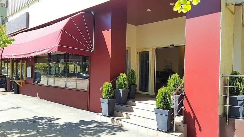 Entrance area with a red awning and potted greenery beside glass doors.
