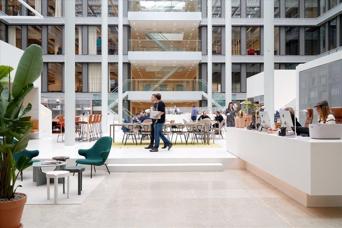 Large sunlit atrium lobby at Paseo de la Castellana, 81, Madrid with white pillars and several lounge areas.