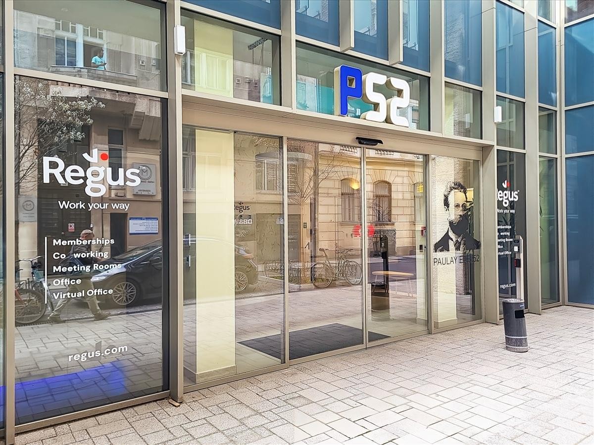 Wide exterior of the modern glass building entrance with sliding doors and building signage.