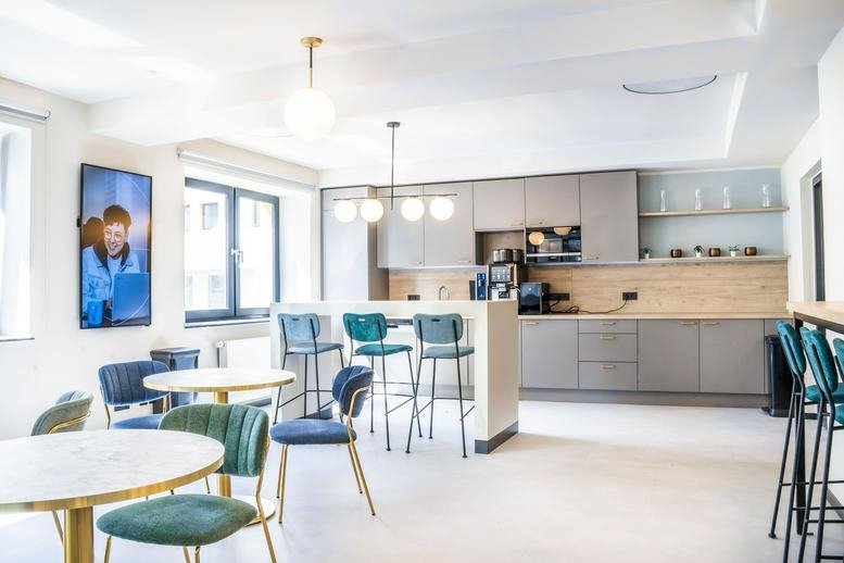 Modern communal kitchen and cafe area with teal chairs and light wood accents.