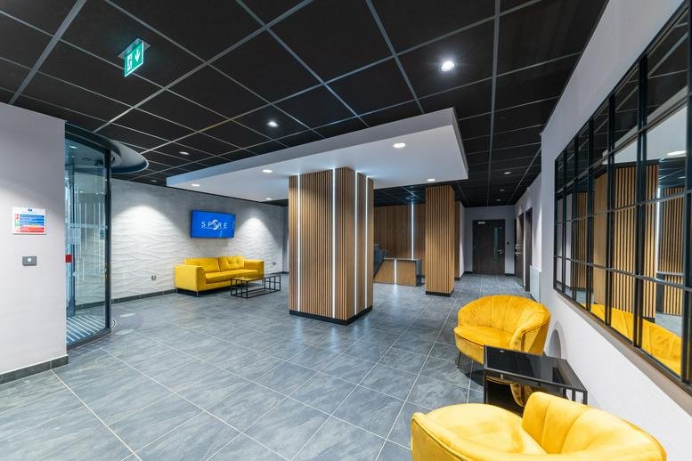 Modern reception lounge at The Spire with yellow velvet chairs and sleek grey flooring.