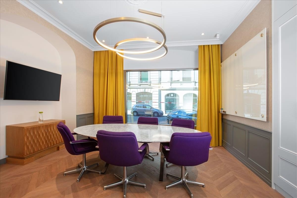 Contemporary meeting room with purple velvet chairs and a unique gold ring chandelier.