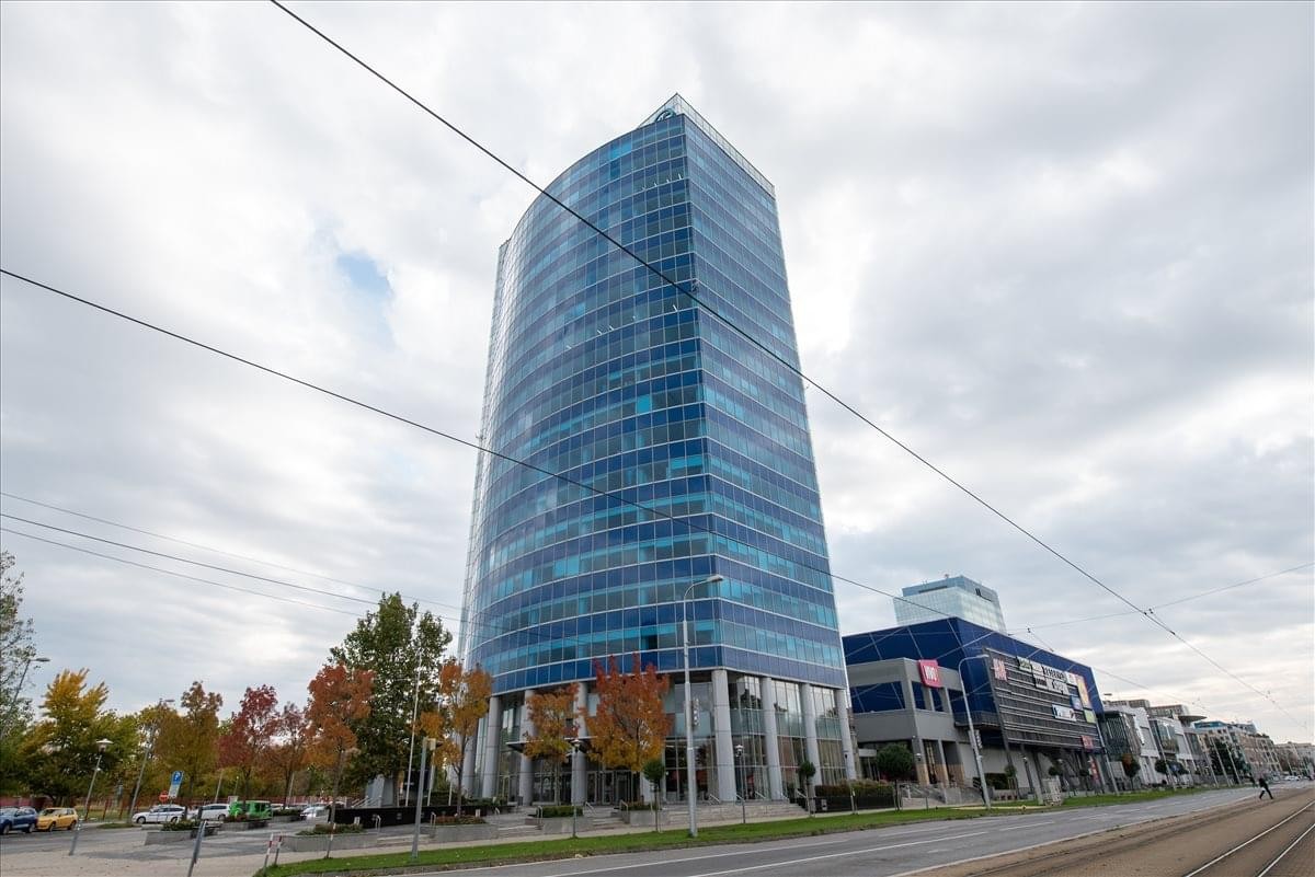 Exterior view of the blue glass-facade Polus Towers high-rise under a cloudy sky.