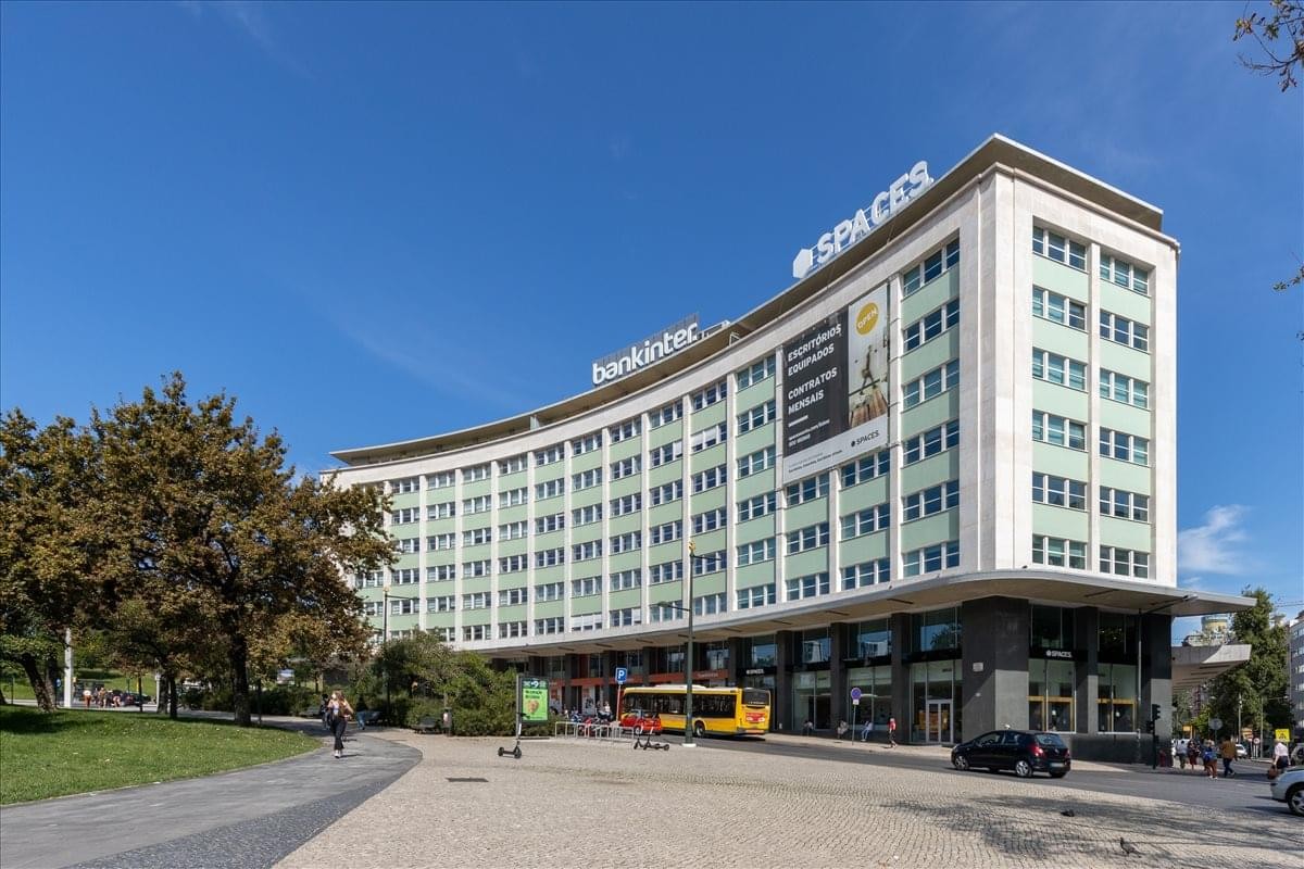 Exterior view of the curved facade of Praça Marquês de Pombal 14 with blue sky and trees.