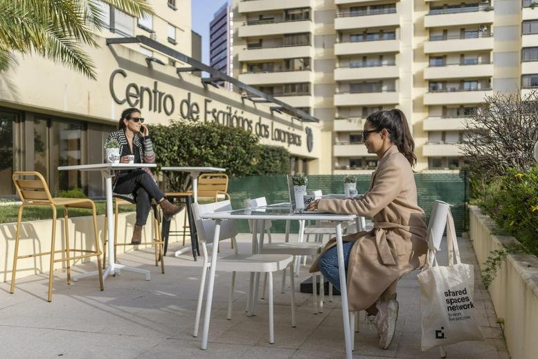 Two people working at white tables on an outdoor terrace at Centro de Escritórios dos Laranjeiras.
