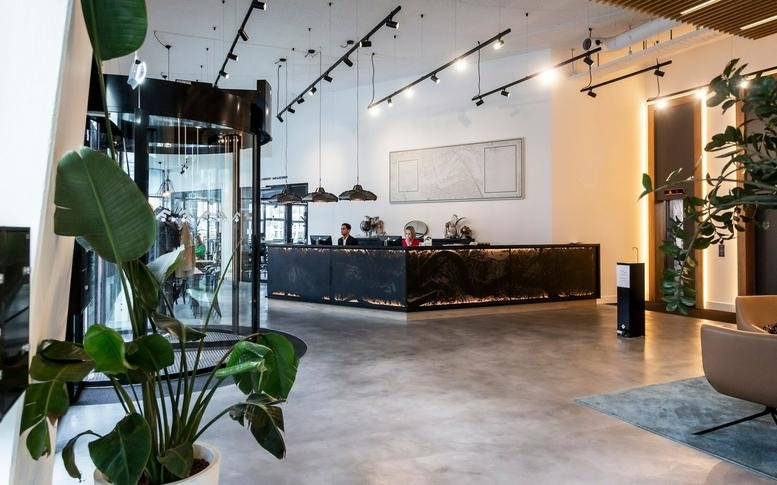 Spacious reception area at Prins Alexanderplein 8 featuring a dark textured desk, high ceilings, and indoor plants.