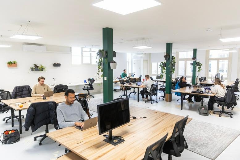 Expansive open-plan office with timber desks and dark green structural pillars.