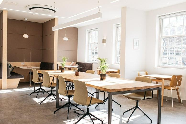 Large open-plan coworking area with long wooden tables and plenty of natural light.