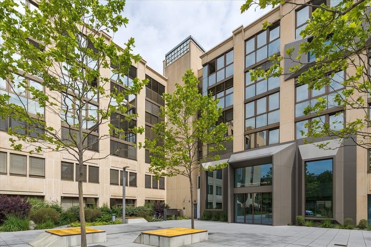 Modern exterior of the office building at Putzbrunner Str. 71-73 with large windows and green trees.