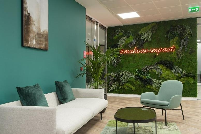 Bright reception lounge at R+, 2 Blagrave Street featuring a green moss feature wall and plush sofa.
