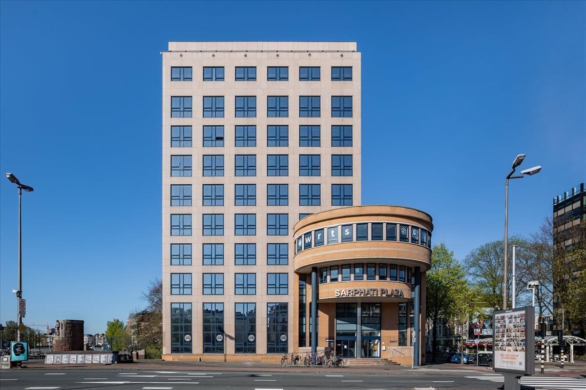 Exterior view of the tan brick building at Rhijnspoorplein 10-38 with its distinct rounded glass entrance.