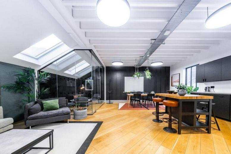 Bright lounge area with a grey sofa, skylights, and a wooden breakfast bar with stools.