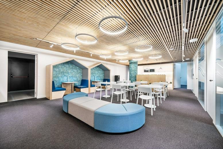 Spacious lounge area with wood-slat ceilings, circular light fixtures, and blue seating pods.